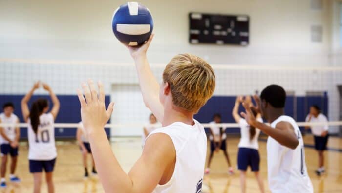 High school student plays a game of team volleyball inside a school gym. AED training in California.
