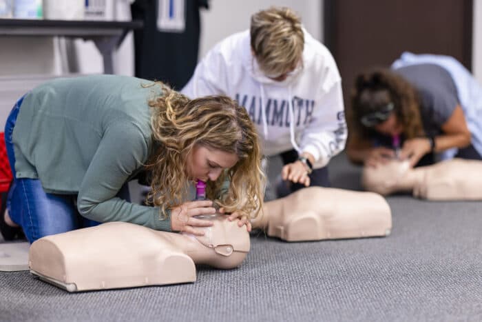 Women practicing CPR on a manikin in a CPR certification class. 