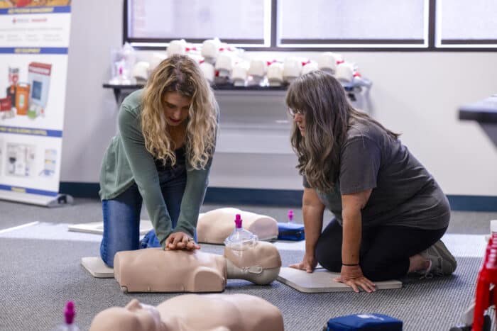 Two women practicing CPR techniques on a manikin. 