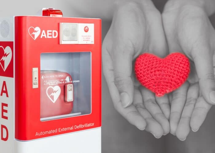 AED machine attached to wall with hands holding heart 
